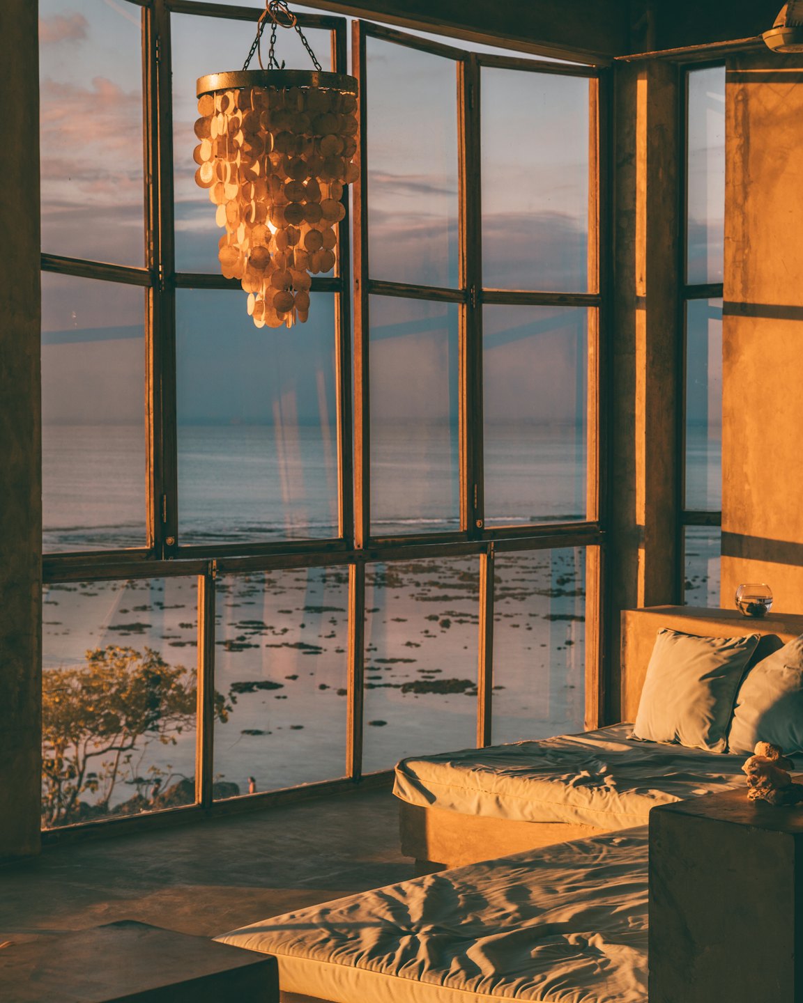 Sunlight streams into a room with ocean views and shell chandelier.