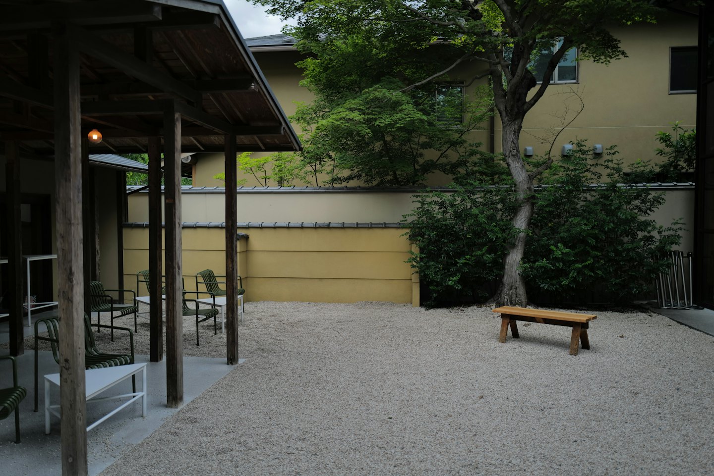 Empty wooden pergola and chairs in a gravel outdoor courtyard.