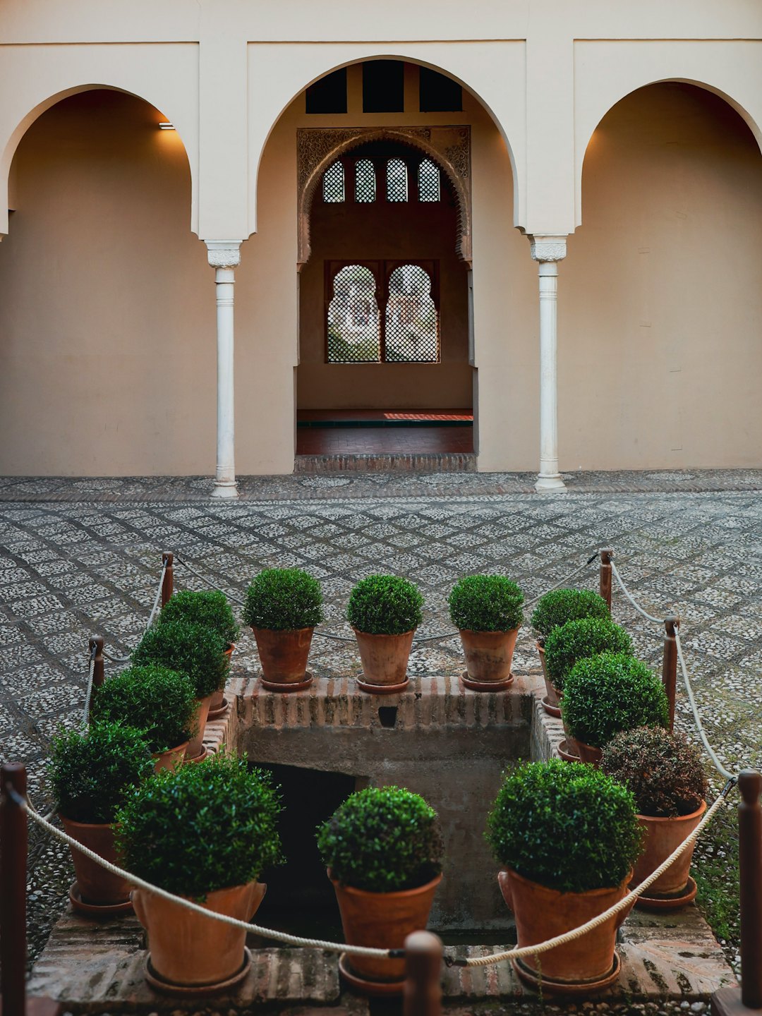 Green shrubs line a water feature within an arched stone courtyard.