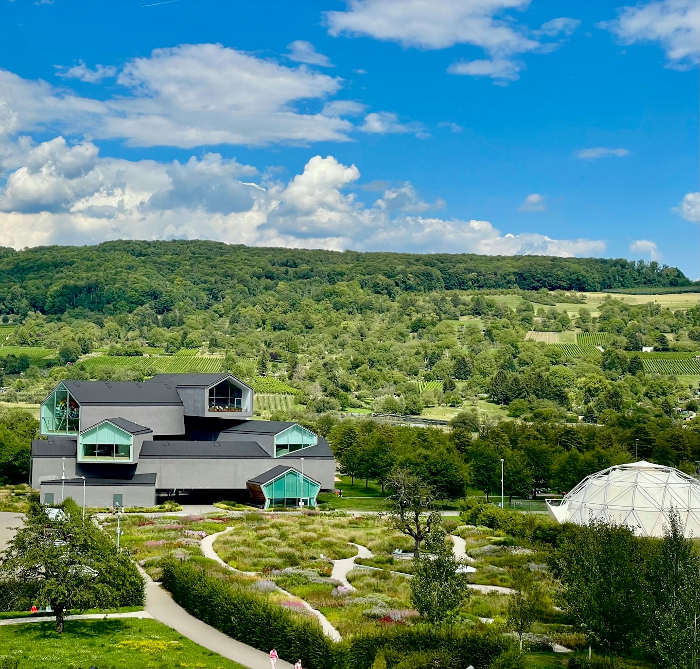 Modern building with a dark facade surrounded by lush gardens.
